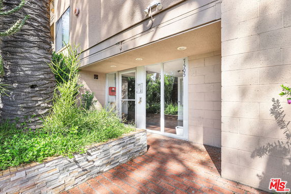Front view of a building entrance with brick walkway and surrounding greenery.