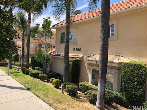 Front view of a beige two-story building with a red-tiled roof and palm trees in front.