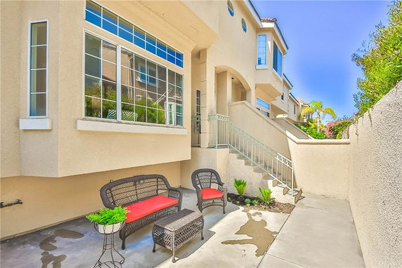 Side view of a beige multi-story house with large windows and an outdoor seating area.