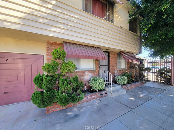Front view of a two-story house with brick and beige siding, featuring red awnings over windows and a small entrance pathway.
