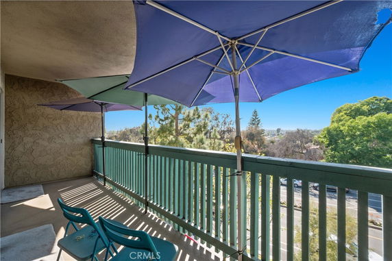 Panoramic view from a balcony with umbrellas and chairs, showing distant trees and urban area.