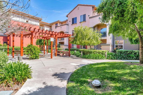 Front view of a multi-story residential building with balconies and a garden pergola.