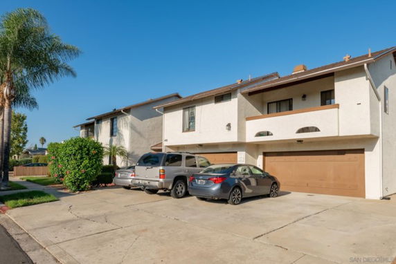 Outdoor parking area in front of a two-story house with garages.