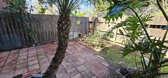 Outdoor area with tiled floor and wooden fence, surrounded by plants.