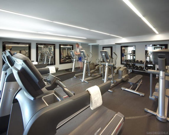 Indoor gym area with various exercise equipment and mirrors on the wall.