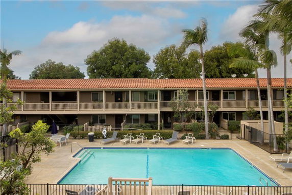 View of a rectangular swimming pool in front of a two-story building with balconies.