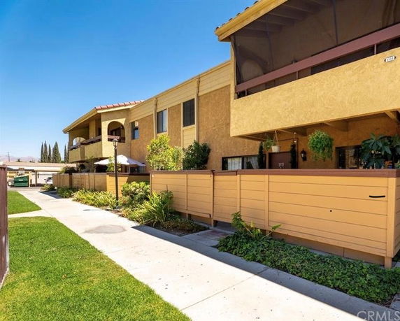 Front view of a multi-story apartment building with balconies and a fenced area.