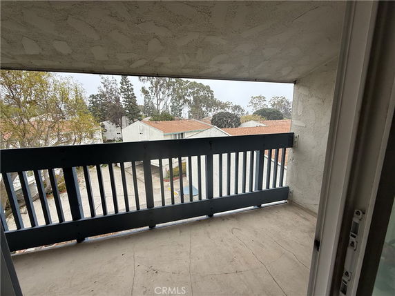 View from a covered balcony overlooking residential buildings and trees.