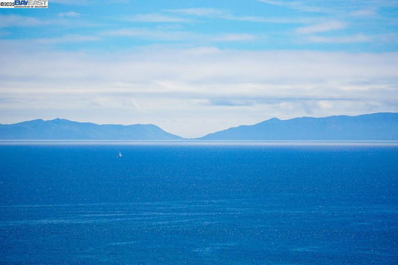Panoramic view of the ocean with distant mountains under a blue sky.