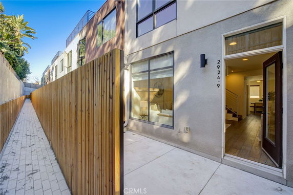 Side view of a modern multi-story building with a pathway and a tall wooden fence.
