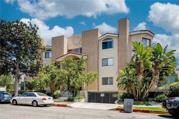 Front view of a multi-story residential building with brick and stucco facade and landscaped entrance.