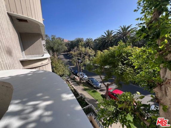 View of a street with parked cars and palm trees as seen from a building.