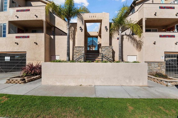 Front view of a multi-story residential building with balconies and palm trees.