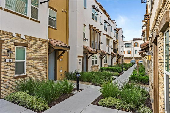 Front view of a multi-story residential building with various entrances and landscaped walkway.