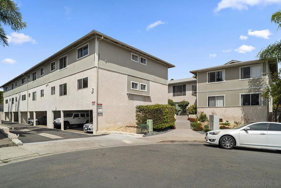 Front view of a multi-story apartment building with covered parking spaces.