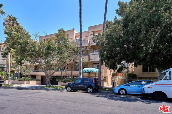 Front view of a multi-story building with balconies and trees in front.