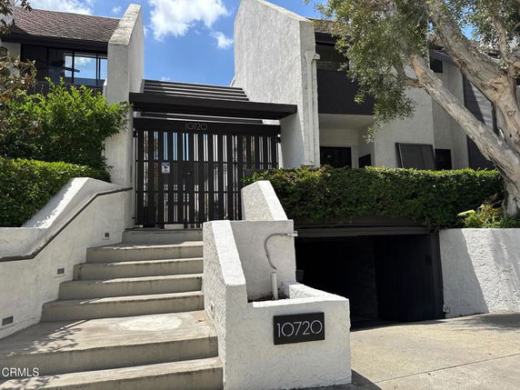 Front view of a residential building with a gated entrance and stairs leading up.