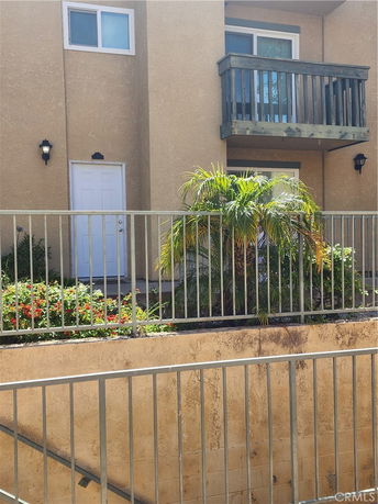 Front view of an apartment building with a balcony and plants.