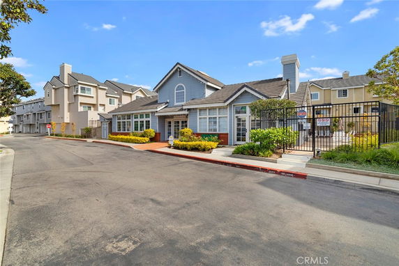Front view of a multi-story residential building with gable roofs and a fenced patio area.