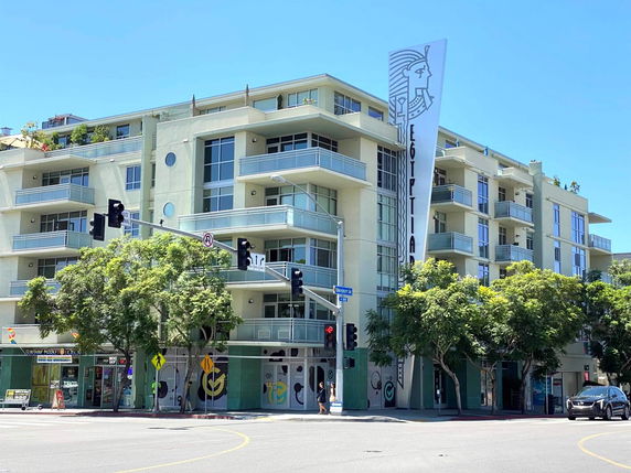 Front view of a multi-story residential building with balconies and a vertical banner on the facade.
