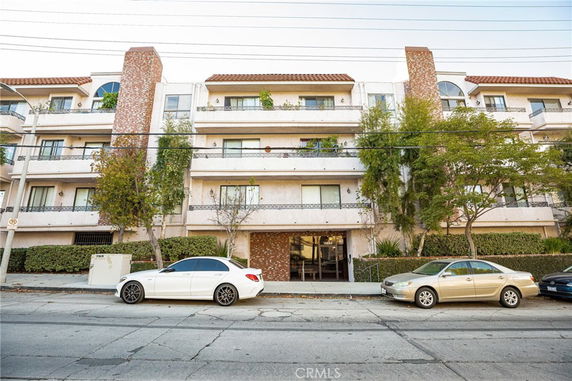 Front view of a multi-story apartment building with balconies and a brick facade.