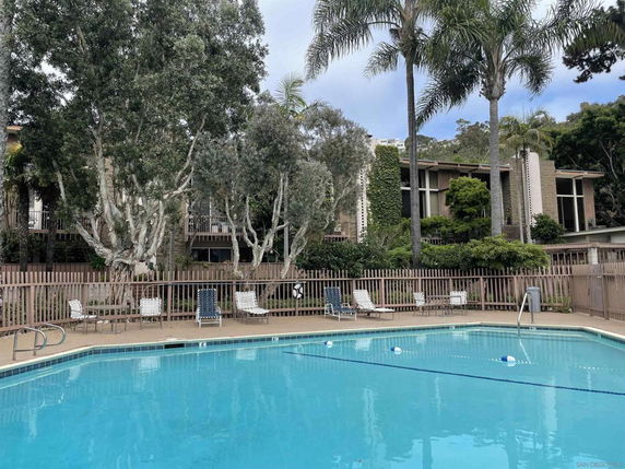 Outdoor swimming pool area with surrounding trees and a multi-story residential building.