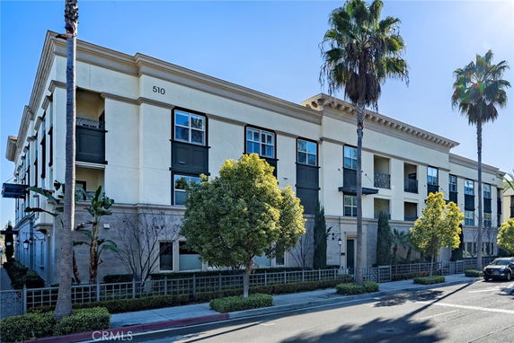 Front view of a multi-story residential building with balconies and palm trees.