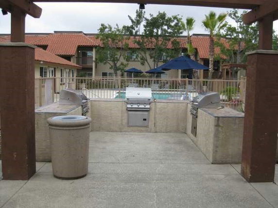 Outdoor area with a barbecue grill setup and view of a swimming pool with umbrellas and chairs in the background.