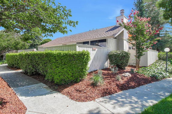 Side view of a single-story house with sloped roof and fenced yard.