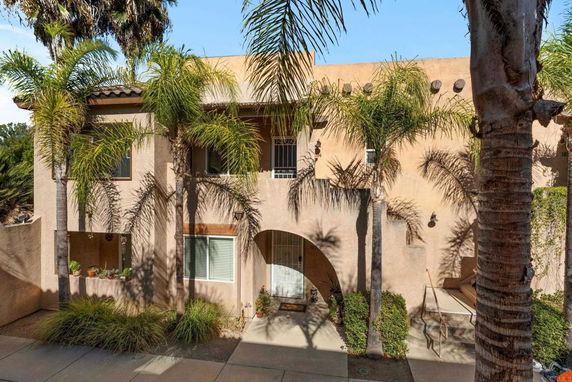Front view of a two-story house with an arched entrance and palm trees.