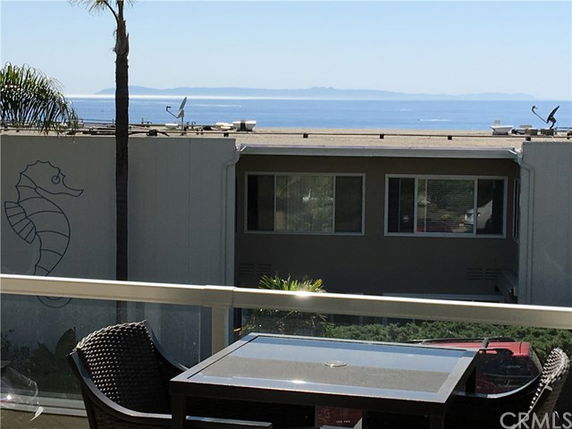 Panoramic view from a rooftop balcony showing a modern building and distant ocean.