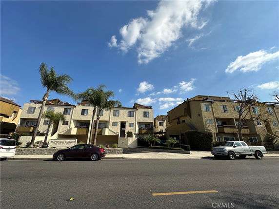 Front view of a multi-story residential building with balconies and palm trees.