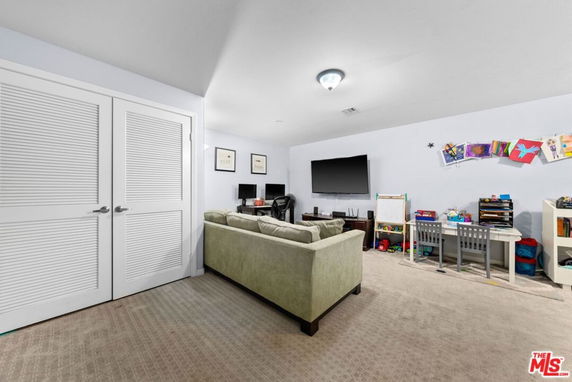 Room with a sofa, TV, desks with chairs, and children's art supplies.
