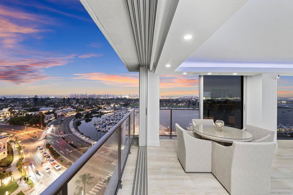 Panoramic view from a balcony overlooking a cityscape and marina at sunset.