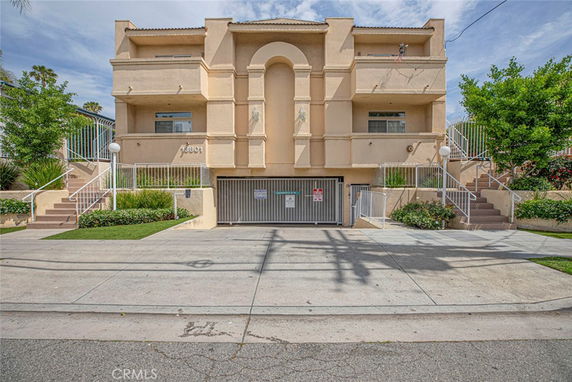 Front view of a multi-story apartment building with staircases on both sides leading to the entrance.
