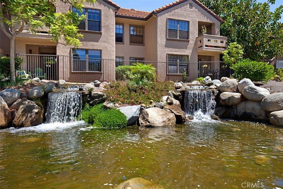 Front view of a two-story house with balconies and a small waterfall in the foreground.