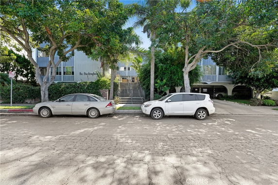 Front view of a multi-story building with trees and parked cars.