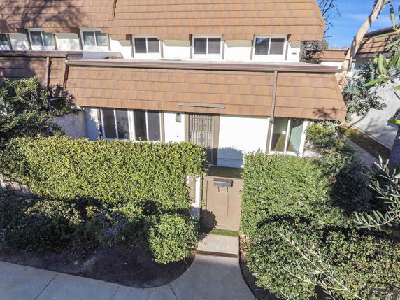 Front view of a two-story house with brown roofing and large windows, surrounded by hedges.