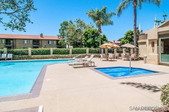 Outdoor swimming pool area with loungers and umbrellas near a residential building.