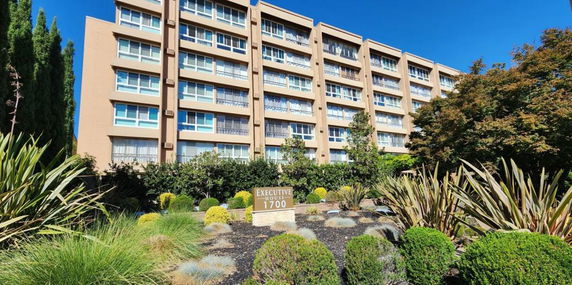 Front view of a multi-story residential building with large windows and a landscaped garden in front.