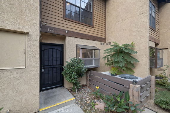 Front view of a beige stucco townhouse with a black door and small garden area.