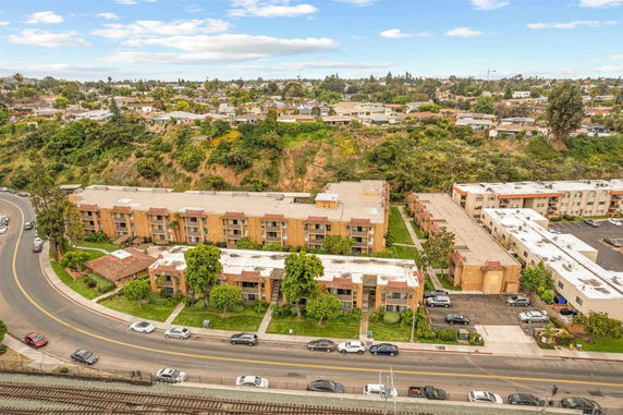 Aerial view of a residential complex surrounded by greenery and a road with parked cars.