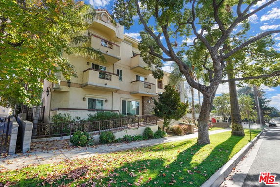 Front view of a multi-story building with balconies and a tree-lined sidewalk.