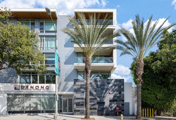 Front view of a modern multi-story building with balconies and a glass facade.