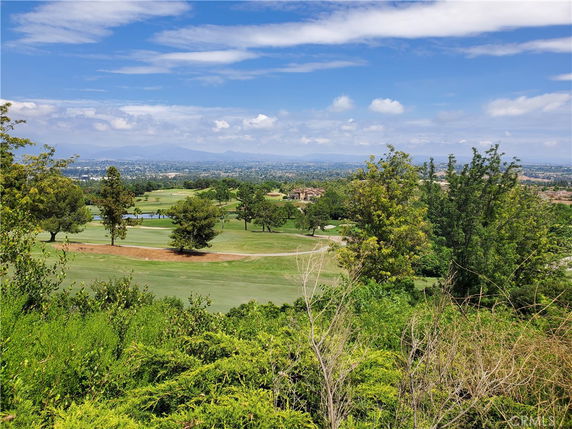 Wide view of a golf course surrounded by trees with distant mountains in the background.