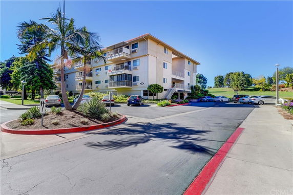Front view of a multi-story apartment building with balconies and parking area.