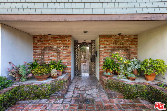Front entrance view of a house with brick walls, potted plants, and a gated doorway.