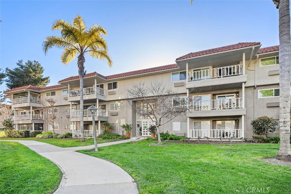 Front view of a three-story apartment building with balconies and a landscaped lawn.