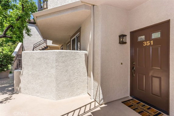 Front view of a building entrance with a brown door marked 351 and surrounding white stucco walls.