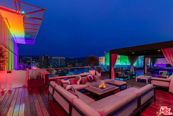 Rooftop with seating area and fire pit, featuring colorful lighting.